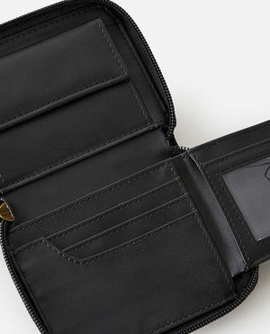 The Rip Curl Wanderer Small Zip Wallet is open, showcasing card slots, a clear ID window, and a coin zippered section. Designed with minimalism in mind, its neatly stitched interior emphasizes organization. The empty wallet's black leather stands out against a white background.