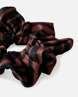 The Rip Curl Sun Tribe Scrunchie, featuring black and dark brown stripes in a lustrous smooth texture, is partially visible against a plain white background.