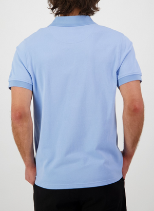 A person with medium-length brown hair wears a Swanndri Highgrove polo crafted from combed cotton pique and black pants, standing with their back to the camera against a plain white background.