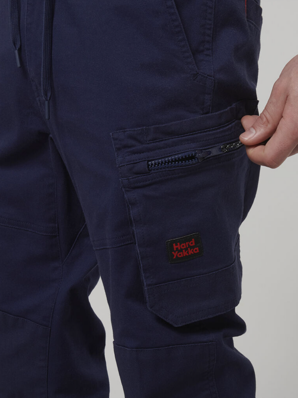 Close-up of someone in dark blue Hard Yakka Tough Maxx Pants with sun protection, featuring a visible zipper pocket and the "Hard Yakka" logo, adjusting the zipper.