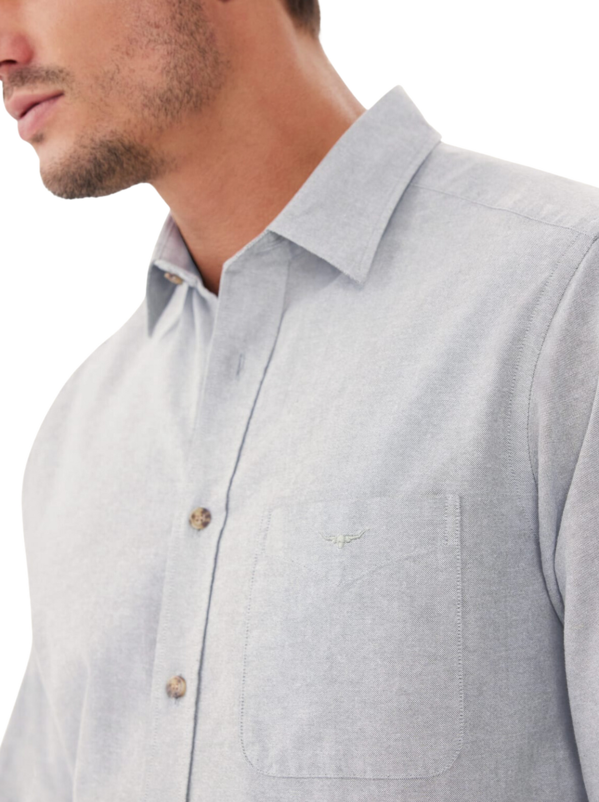 A man models the RM Williams Collins Shirt in light grey cotton paper poplin with a front pocket and subtle longhorn embroidery. Only his lower face, neck, and upper body are visible against a white background.