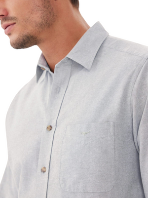 A man models the RM Williams Collins Shirt in light grey cotton paper poplin with a front pocket and subtle longhorn embroidery. Only his lower face, neck, and upper body are visible against a white background.