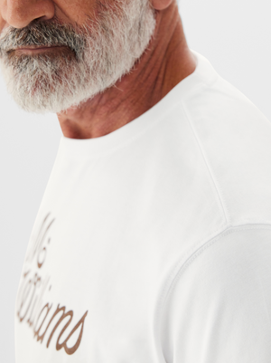 Close-up of an older man with a white beard, wearing an RM Williams R.M.W Script T-Shirt. The background is light gray.