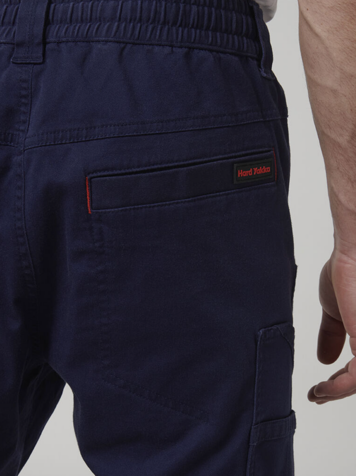 Close-up of someone in navy blue Hard Yakka Tough Maxx Pants featuring an elastic waistband and multiple pockets, with the red and black logo above the right back pocket. These pants are designed for durability and practicality on the job.