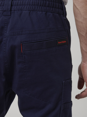 Close-up of someone in navy blue Hard Yakka Tough Maxx Pants featuring an elastic waistband and multiple pockets, with the red and black logo above the right back pocket. These pants are designed for durability and practicality on the job.
