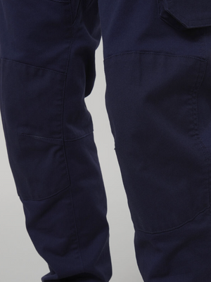 Close-up of a person wearing Hard Yakka Tough Maxx Pant in durable dark navy blue featuring textured fabric, detailed stitching, seams, and a pocket flap, set against a plain light gray background.