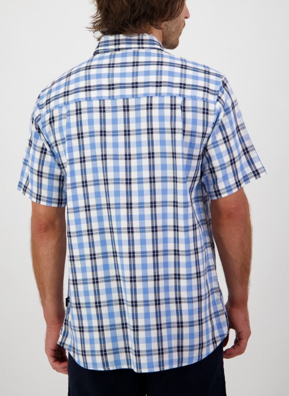 A person is shown from the back wearing a blue and white Swanndri Russell Shirt, featuring short sleeves, relaxed fit, and 100% cotton fabric, standing against a plain white background.