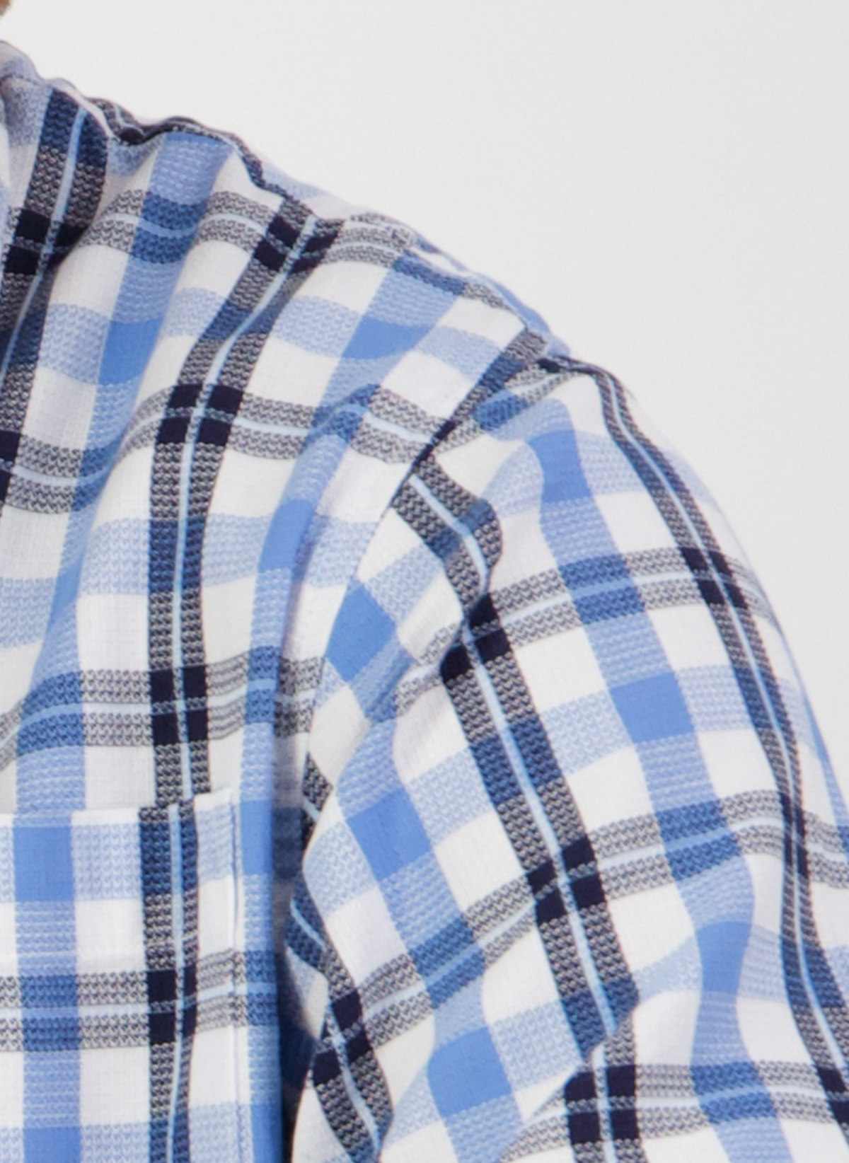 Close-up of the Swanndri Russell Shirt in blue, black, and white plaid with a front pocket. Made from 100% cotton for a relaxed fit, shown against a light background featuring part of the wearer's shoulder and chest.
