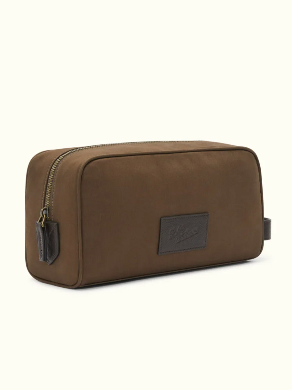 The RM Williams Hawkesbury Washbag is a rectangular brown travel washbag with a gold zipper, leather pull tab, and logo patch. Made of waxed cotton with a waterproof lining, it features a simple minimalist design.