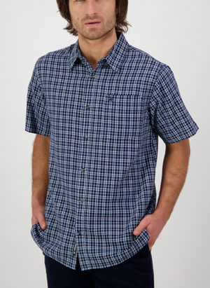 Someone in a relaxed fit Swanndri Russell Shirt, featuring 100% cotton with short sleeves and a dark blue and white checkered design, stands with hands in pockets against a plain white background.