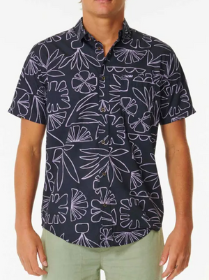 A person wearing a Rip Curl SWC Short Sleeve Shirt featuring a white abstract floral pattern and light green pants stands against a plain white background.