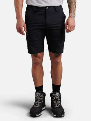 Wearing King Gee Trademark Cargo Shorts in black, a light grey t-shirt, black crew socks, and black hiking boots, a person stands against a plain white background with relaxed arms and a visible tattoo on one arm.