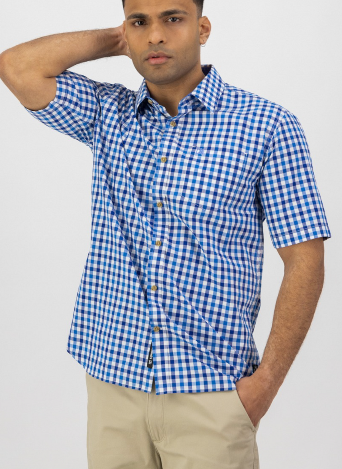 A man poses against a plain white background wearing the Swanndri Moreau Short Sleeve Shirt, featuring a blue and white check pattern, tailored fit, and crafted from 100% cotton.