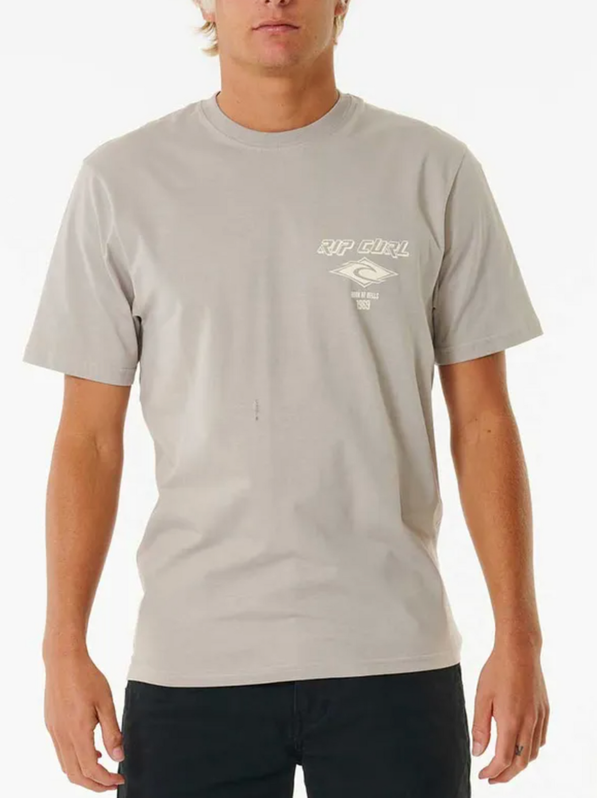 Someone wearing the Rip Curl Fade Out Icon Tee in light grey, featuring a small white logo and text on the left chest, styled with black pants against a plain white background.