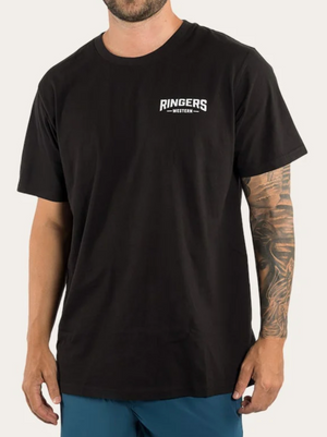A person wearing a Ringers Western Squadron Loose Fit 100% Cotton black T-shirt with short sleeves stands against a plain background. The T-shirt features a white text logo on the upper left side. They have a tattoo sleeve on their right arm and are wearing blue pants.