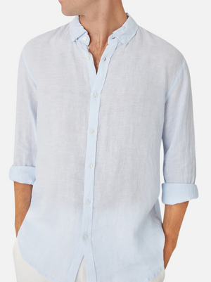 A person wears the Industrie The Tennyson Linen Shirt in light blue, sleeves rolled up. The image focuses on the upper body with their head turned to the side, showcasing the shirt's relaxed fit and casual style.