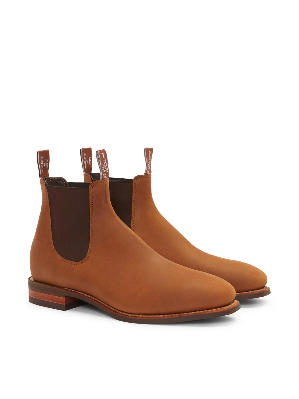 The RM Williams Comfort Craftsman Boot is a handmade nubuck leather brown Chelsea boot featuring elastic side panels, pull tabs, a sleek design, and low wooden heels. These boots are elegantly showcased against a crisp white background.