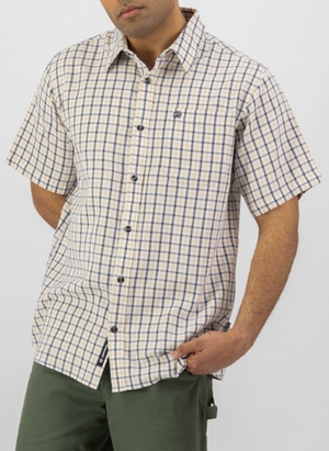 A person wearing the Swanndri Russell Shirt, a relaxed fit, short-sleeve 100% cotton button-up in beige and navy check, and green pants stands with one hand in their pocket against a plain white background.