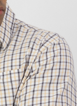 Close-up of a person wearing the Swanndri Russell Shirt, shown from the shoulders up against a plain white background. The shirt features a yellow and black checkered pattern, relaxed fit, and is made from 100% cotton. Face partially visible on the left.