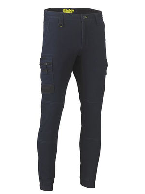 The Bisley Flex & Move Stretch Denim Cargo Cuffed Pant features multiple cargo pockets, a fitted design, reinforced knees, ankle zippers, and “Bisley” branding on the waistband for practical and stylish storage.