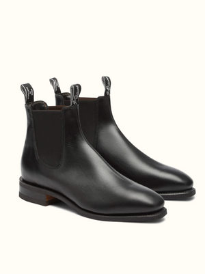 Introducing the RM Williams Comfort Craftsman Boot, a pair of black pull-up leather Chelsea boots featuring elastic side panels and convenient pull tabs adorned with white text. These sleek boots boast a slight shine, wooden soles, and rounded toes. The interior lining is brown, adding to their sophisticated appeal.
