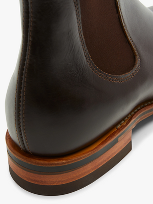 Close-up of the back heel of an RM Williams Dynamic Flex Craftsman Boot in dark brown Yearling leather, showcasing visible stitching. The boot has a wooden sole with a dark rubber layer at the bottom and features a Dynamic Flex system, including a dark brown elastic gusset on the side, typical of high-quality elastic-sided boots.