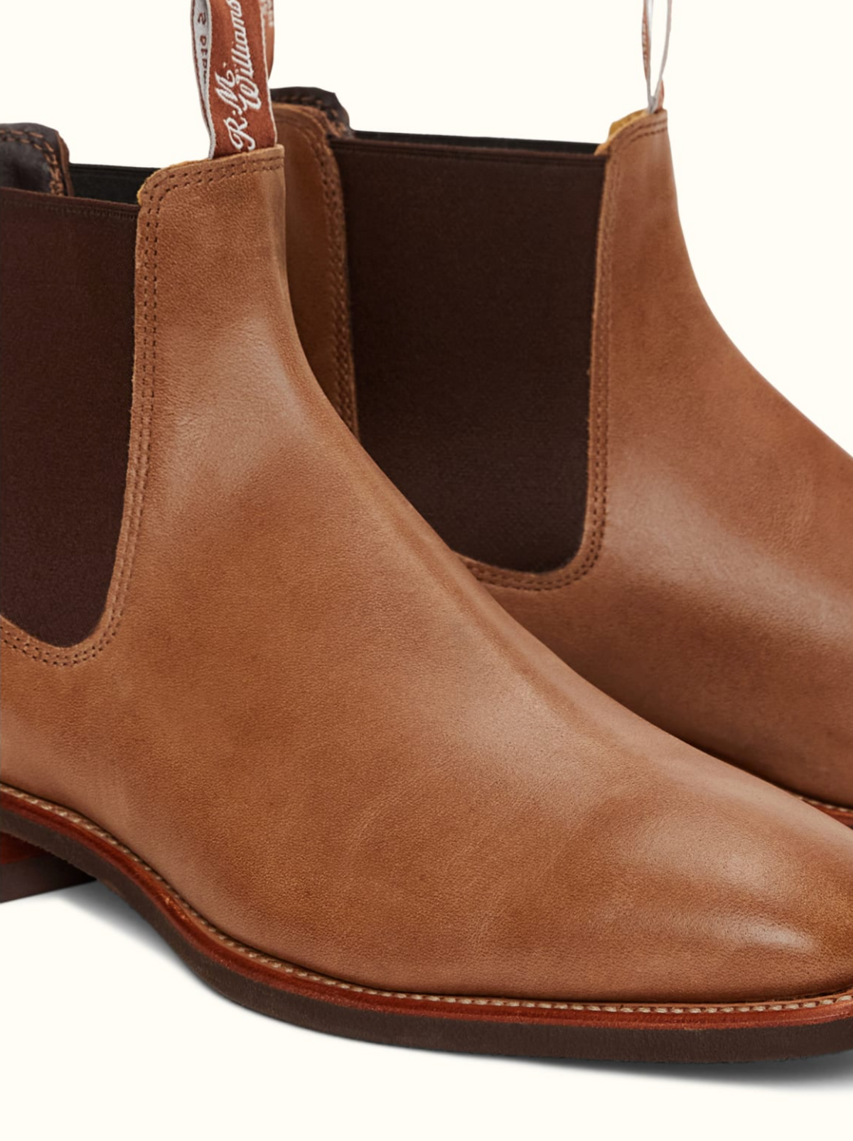 A close-up image of the RM Williams Comfort Craftsman Boot in brown leather. These Chelsea boots feature elastic side panels with pull tabs and are placed on a light background. The smooth, polished leather and classic chisel square toe design enhance their timeless simplicity.