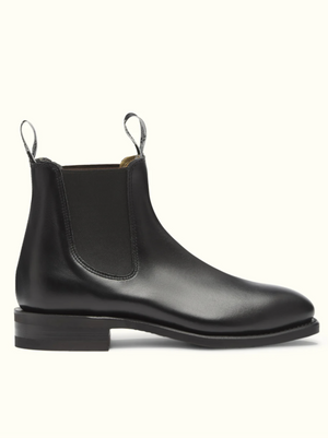 The RM Williams Comfort Craftsman Boot is presented on a plain light background, showcasing its black leather Chelsea design with a smooth finish. It features durable rubber soles, elastic side panels, pull tabs at both the front and back, and a sleek, low wooden heel.