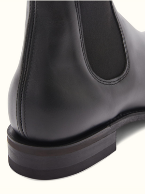 Close-up image of the back of an RM Williams Comfort Craftsman Boot in black leather, focusing on the smooth leather surface and stitching details. The image highlights the heel, durable rubber sole, and elastic side panel characteristic of these boots.