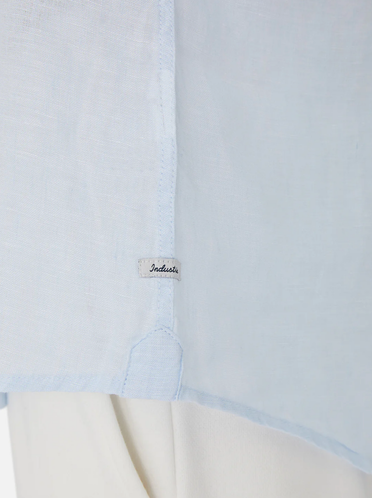 Close-up of the Industrie The Tennyson Linen Shirt in light blue, featuring a subtle side seam tag, styled over white pants for a timeless look.