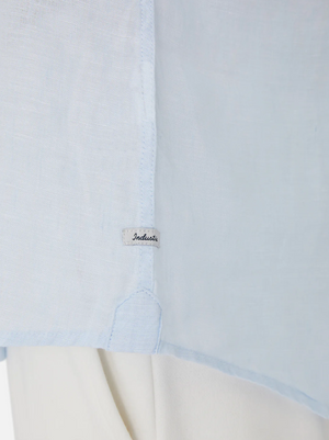 Close-up of the Industrie The Tennyson Linen Shirt in light blue, featuring a subtle side seam tag, styled over white pants for a timeless look.