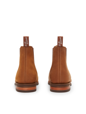 The back view of RM Williams' Comfort Craftsman Boot in brown nubuck leather features pull tabs, a smooth finish, and a layered wooden sole, showcasing artisanal craftsmanship and contemporary style.