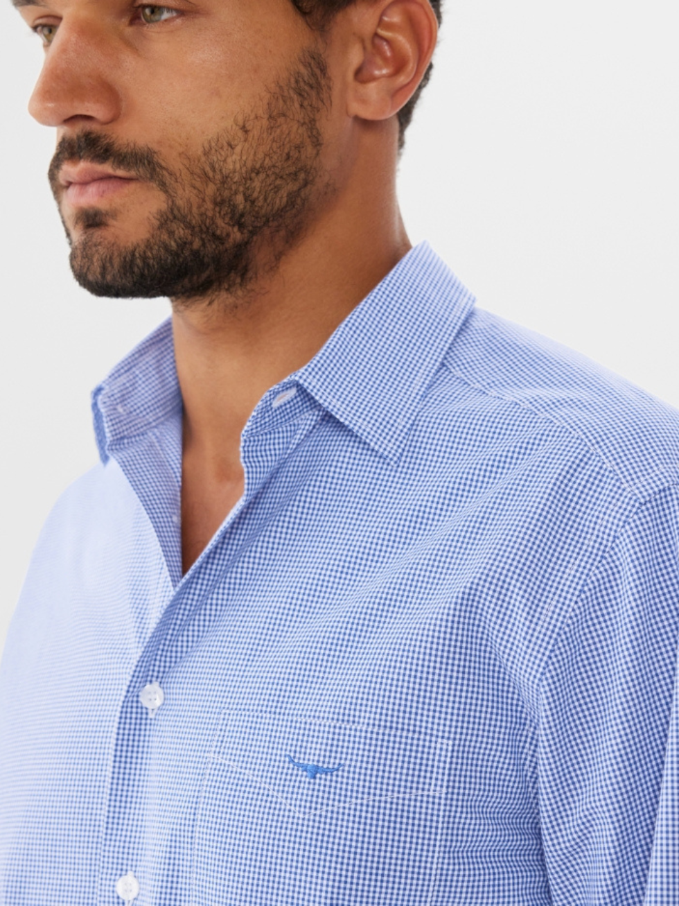 A man with a short beard wears the RM Williams Coalcliff Shirt, a blue and white checkered 100% linen button-up with longhorn embroidery on the chest pocket, standing against a plain white background.