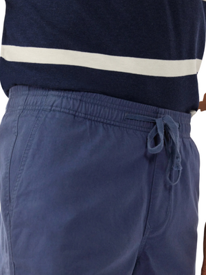 Close-up of a person wearing RM Williams R.M.W Rugby Shorts in blue and a dark blue shirt with a white horizontal stripe across the chest. The focus is on the waist area, showcasing the tied drawstring and stretch cotton twill fabric texture of the shorts, ideal for achieving a relaxed style.