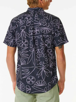 Someone is seen from the back wearing a Rip Curl SWC Short Sleeve Shirt featuring a white abstract floral pattern and standard fit, paired with light green shorts.