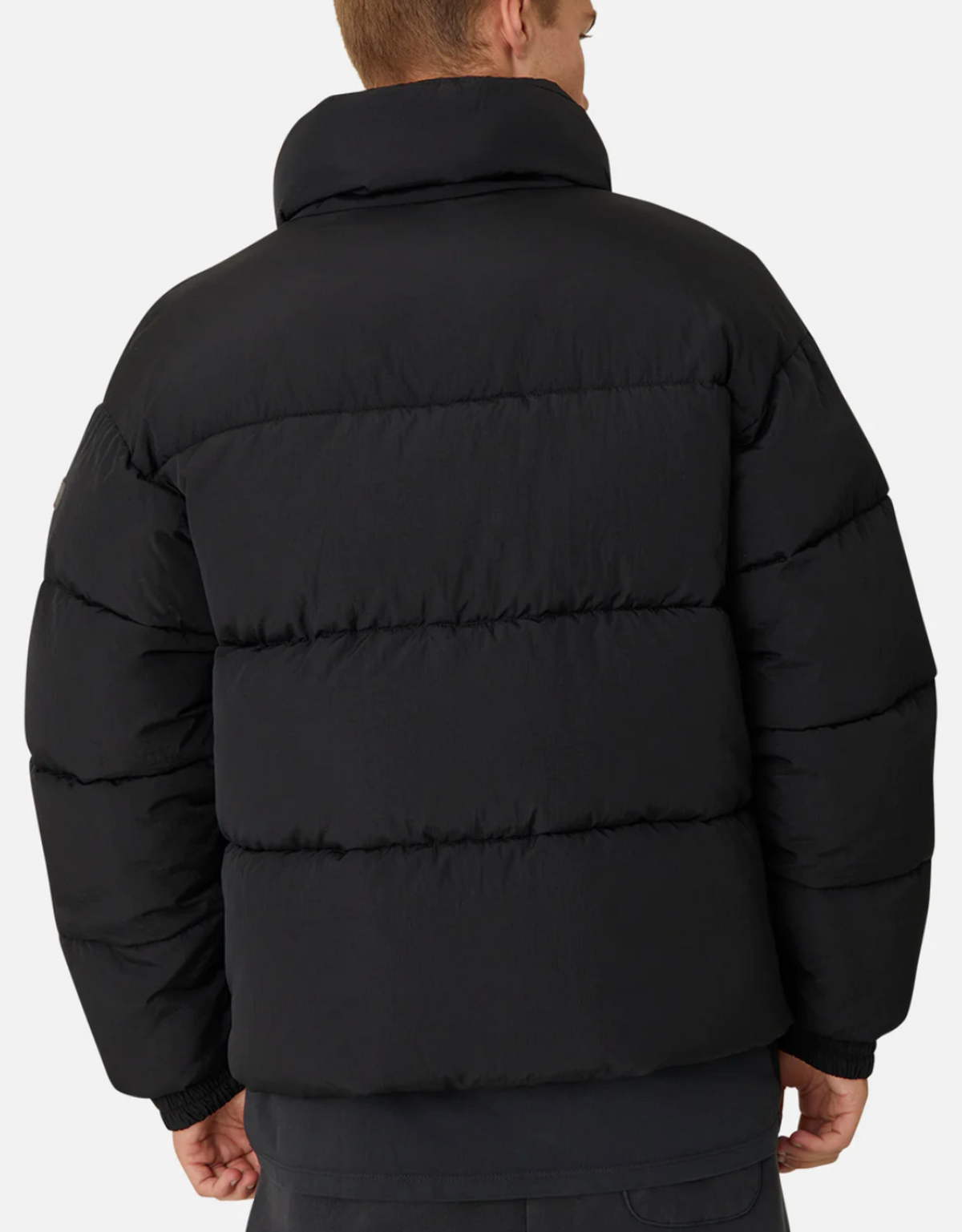 A person is seen from behind in an Industrie The Regent Puffer Jacket, black with quilted padding and a high collar, featuring horizontal stitching against a plain white background.