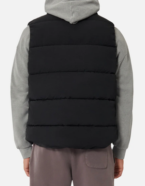 A person wearing an Industrie The New Hanam black puffer vest with quilted padding over a gray hoodie is seen from behind, paired with brown pants against a plain white background.