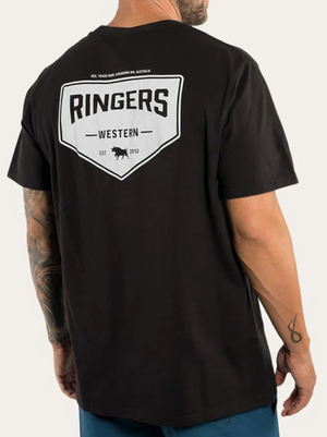 A man with tattooed arms wears a black Ringers Western Squadron Loose Fit T-Shirt, made from 100% cotton. The shirt displays the "Ringers Western" logo on the back, featuring a shield with the text "Ringers Western" and an image of a cow. Below the shield, it reads "Est 2012".