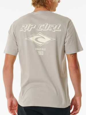 A person seen from the back in a light gray Rip Curl Fade Out Icon Tee, made of cotton. The t-shirt displays "RIP CURL," a logo, and "BORN AT BELLS 1969"—offering classic throwback style.
