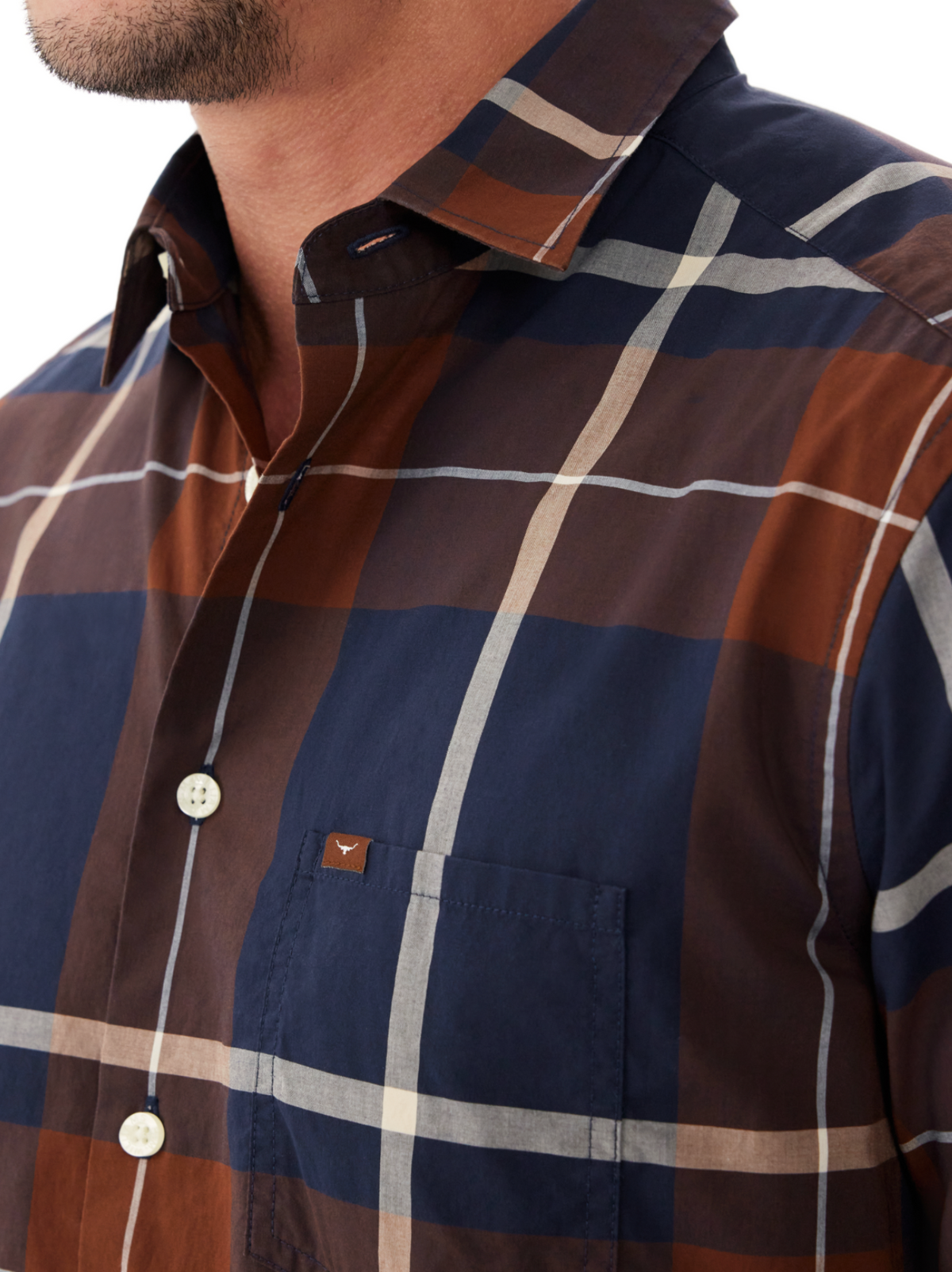 Close-up of a man in the RM Williams Coalcliff Shirt with large navy blue, brown, and white plaid, longhorn embroidery on the pocket, and white buttons. His face is partly visible with a trimmed beard.