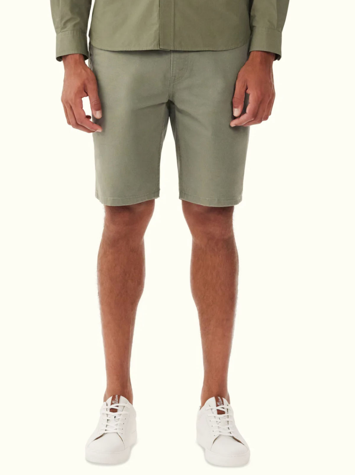 A person is wearing a green shirt paired with RM Williams Nicholson Shorts in premium stretch cotton, standing straight. They have white sneakers on against a white background, highlighting the smart-casual outfit from waist to shoes.