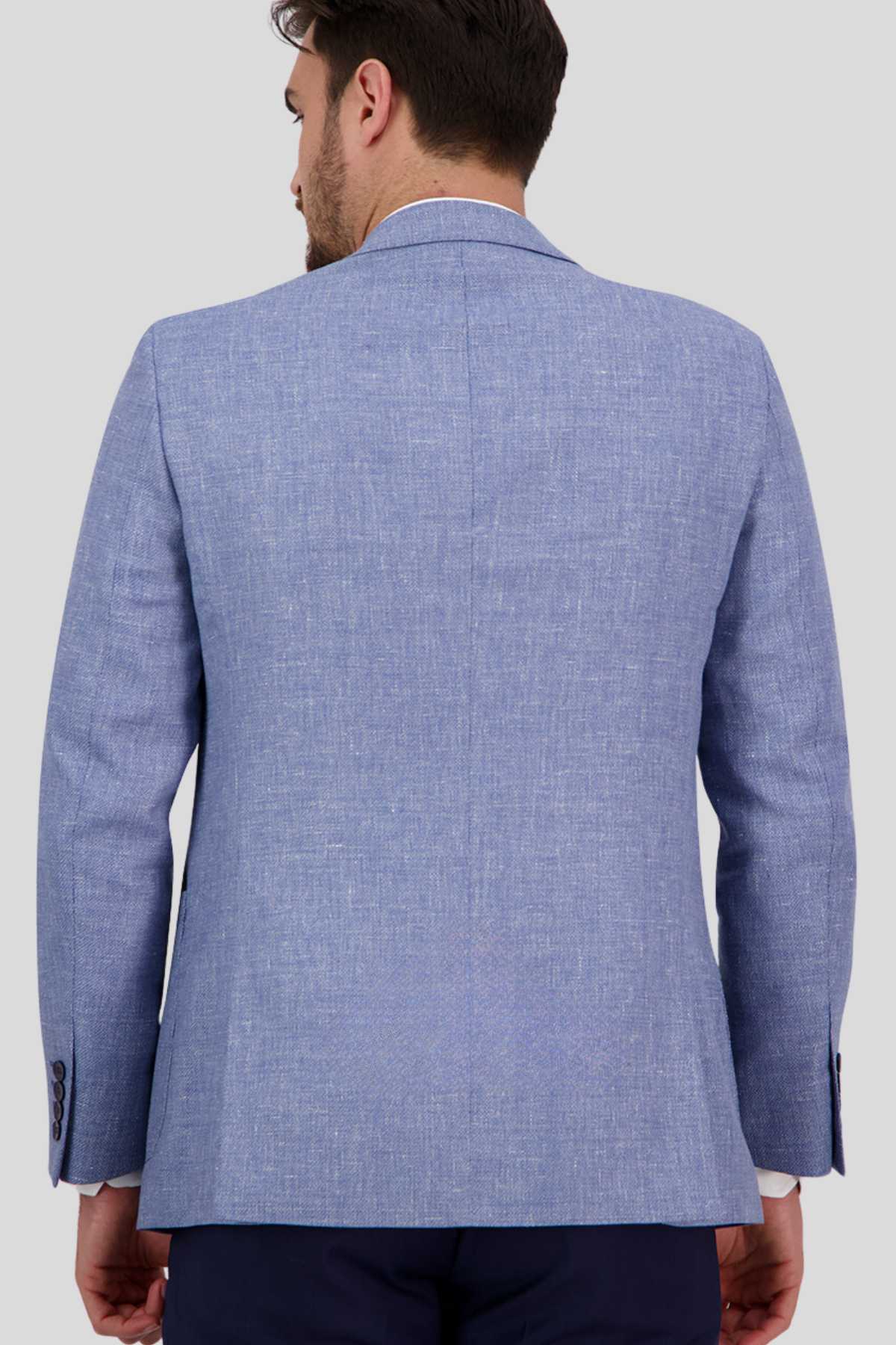 A person with short dark hair, seen from the back, is wearing a Bruton Asher Linen Blazer in light blue with a subtle textured pattern. The contemporary fit blazer includes a single center vent and four buttons on each cuff. They are pairing it with dark pants against a plain gray background.