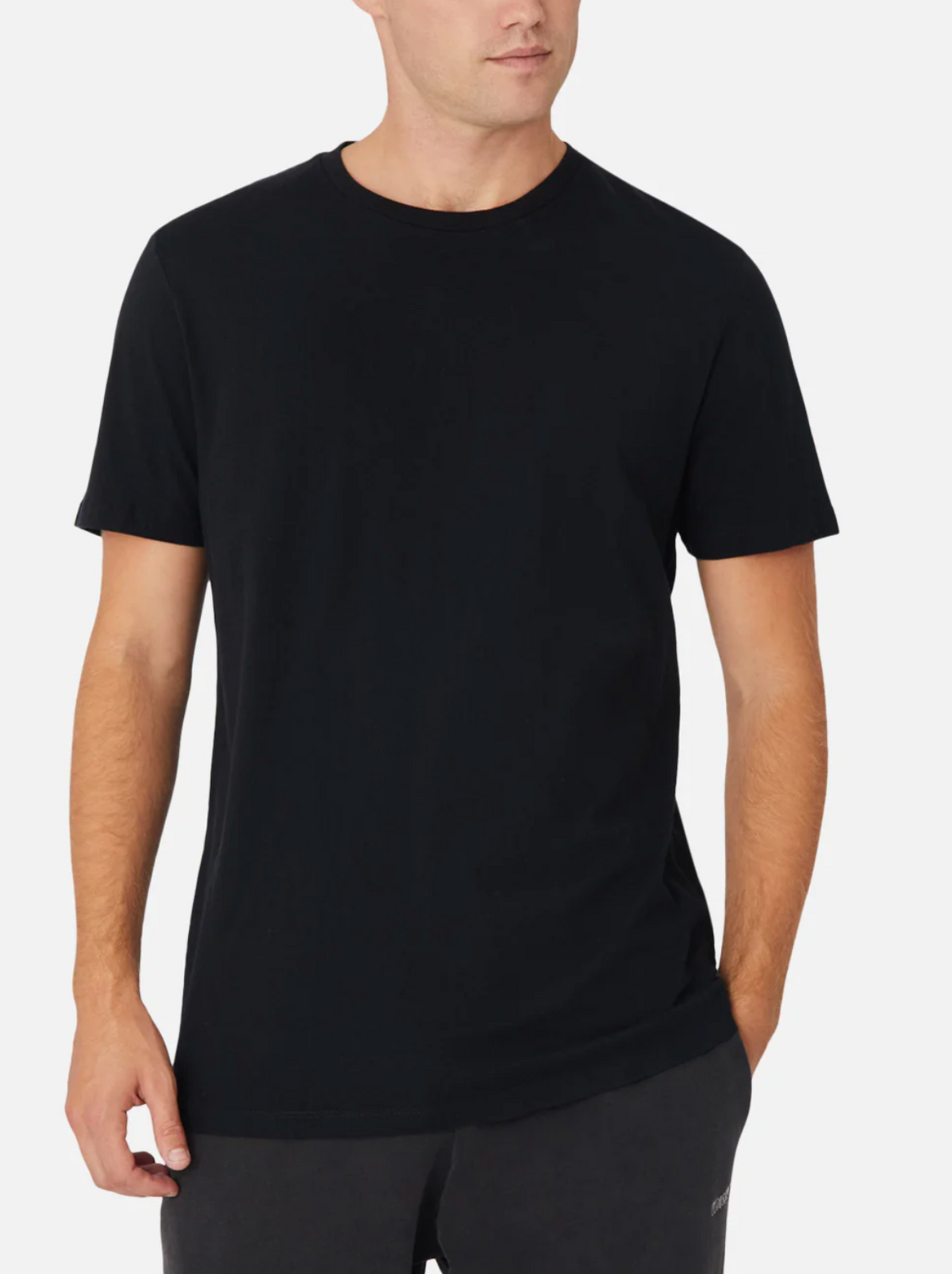 A man wearing the Industrie The Basic Crew Tee in classic fit 100% cotton and dark pants stands with one hand in his pocket, looking slightly to the side against a white background.