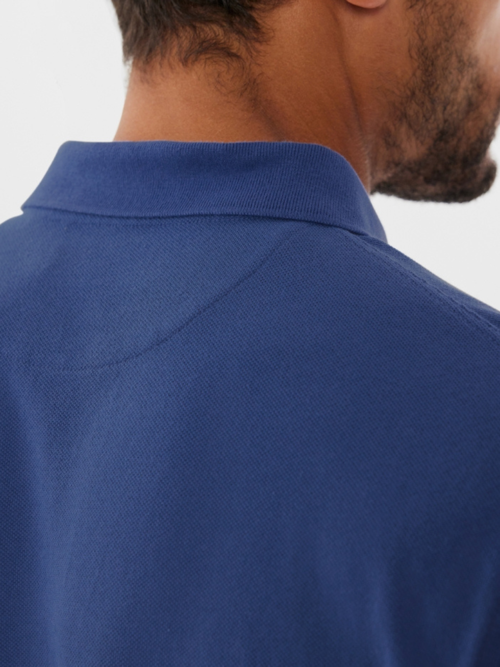 Close-up of the back and side of a man's neck and shoulder, wearing the RM Williams Rod Polo in blue cotton pique. Only part of his face and short hair are visible.