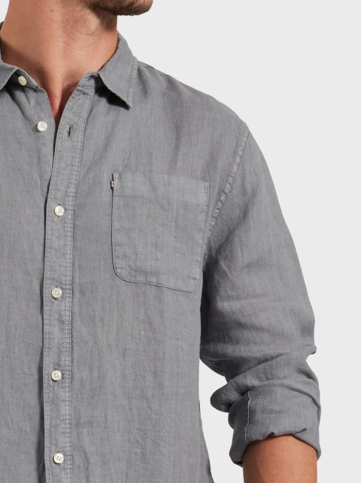 A man in a stylish light gray Academy Brand Hampton Linen Shirt with long sleeves, chest pocket, and rolled-up cuffs. The image is cropped at the neck and mid-torso.