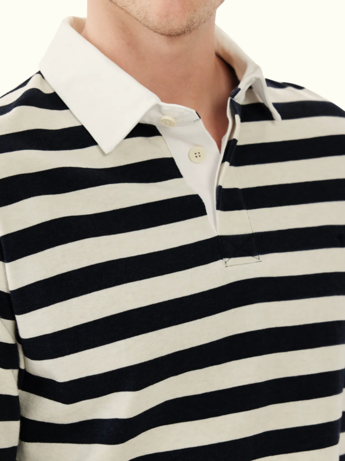 A person wearing the RM Williams Tweedale Rugby: a collared, long-sleeve shirt with black and off-white horizontal stripes, white cotton twill collar, heavyweight jersey knit fabric, and a partially unbuttoned placket. Only upper torso is visible.
