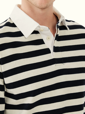 A person wearing the RM Williams Tweedale Rugby: a collared, long-sleeve shirt with black and off-white horizontal stripes, white cotton twill collar, heavyweight jersey knit fabric, and a partially unbuttoned placket. Only upper torso is visible.