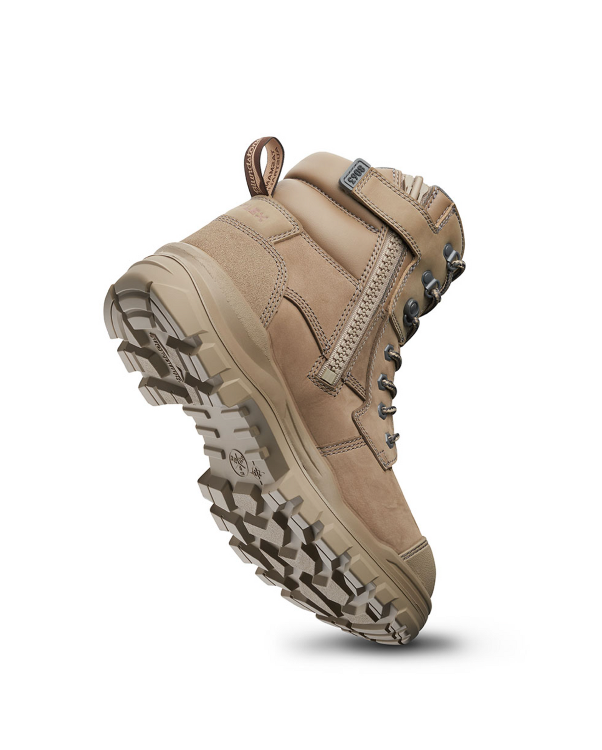 The Blundstone RotoFlex 8063 Zip Sided Safety Boot in light brown nubuck leather is depicted from a low angle, emphasizing its rugged, textured sole. This water-resistant safety boot includes metal eyelets, secure laces, padded ankle support, and a convenient loop at the back for easy wear. The sole is engineered to provide traction on various terrains.