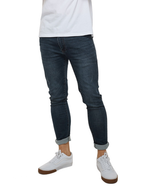 A person wearing Industrie The Denim Drifter NC Pant, skinny fit and cuffed at the ankles, paired with a white T-shirt and white sneakers with brown soles. The photo focuses on the lower body, cropped at the shoulders.