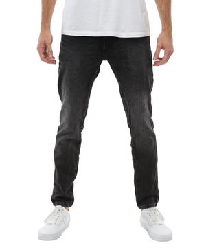A person wearing a white t-shirt, Industrie The Denim Drifter NC Pant in black faded skinny fit, and white sneakers is standing upright with their arms relaxed at their sides against a white background. The person's upper body is not visible in the image.